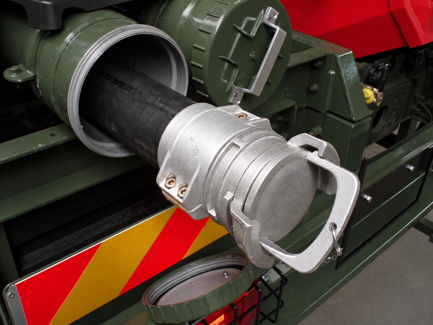 Metal hose coupling with a fitted cap and retaining chain, stowed in a green protective tube.