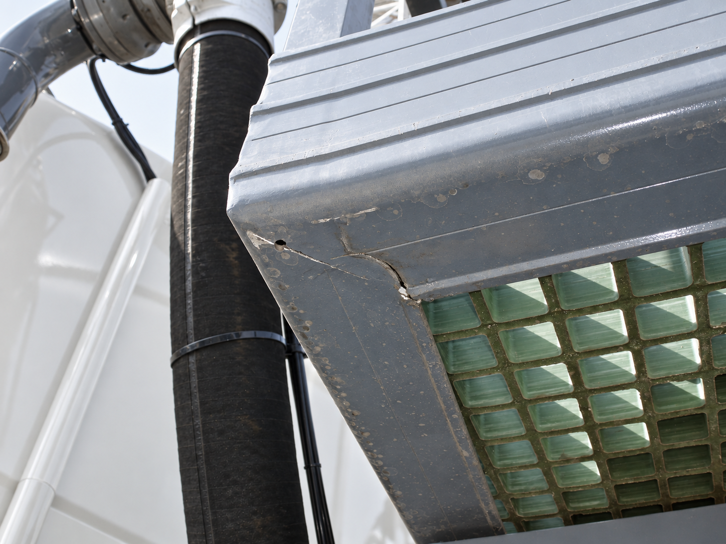 Visible cracking at the corner of a metal frame beside a hose and platform grating.
