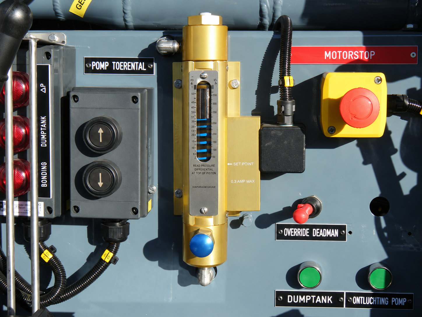 Vertical differential-pressure gauge mounted beside labelled controls and an emergency-stop button.
